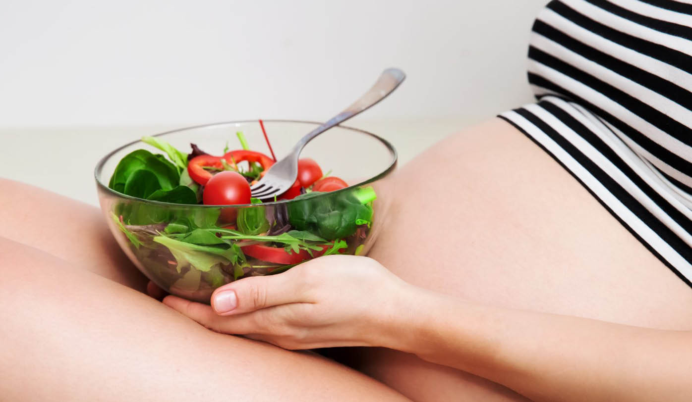 Eine schwangere Frau isst einen Salat mit Tomate und Paprika.