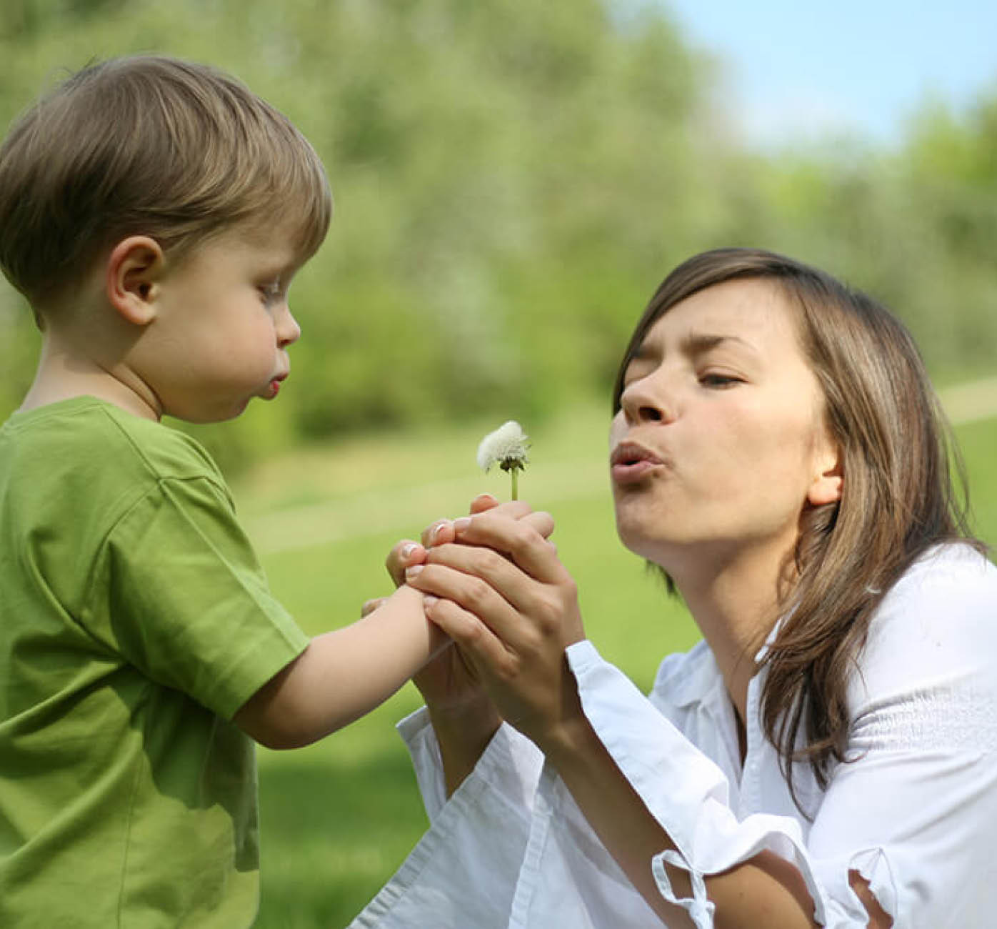 Mutter und Sohn pusten zusammen auf eine Pusteblume.