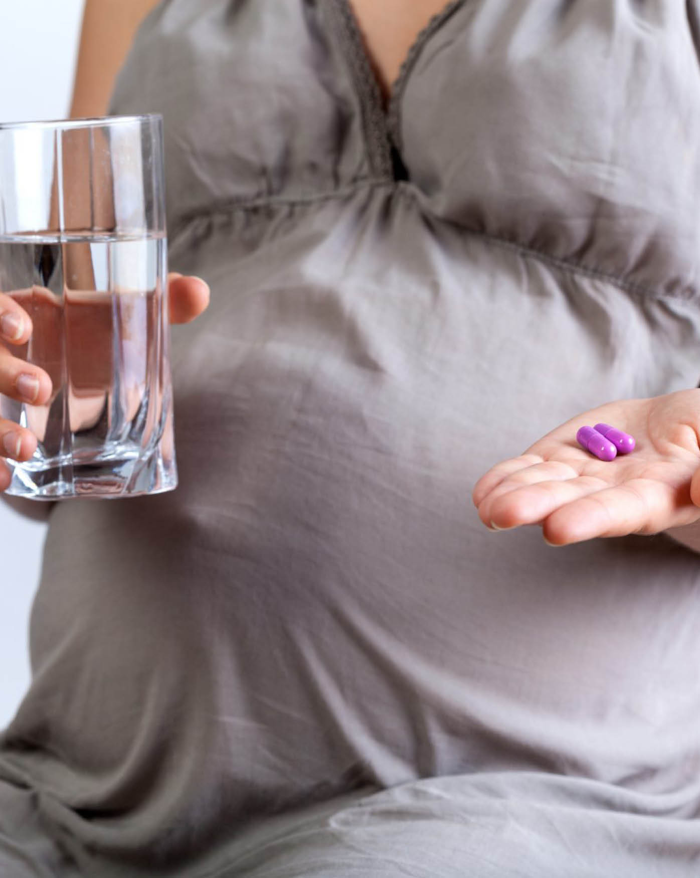 Eine schwangere Frau nimmt Medikamente mit einem Glas Wasser ein.