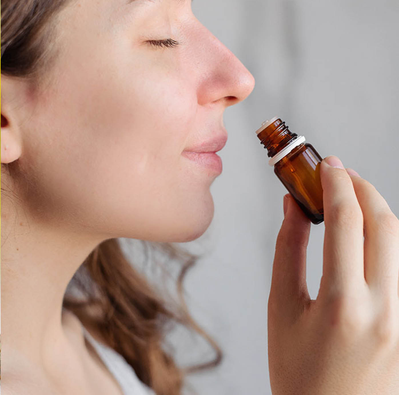 Eine junge Frau riecht an einem Fläschchen mit Aromaöl.