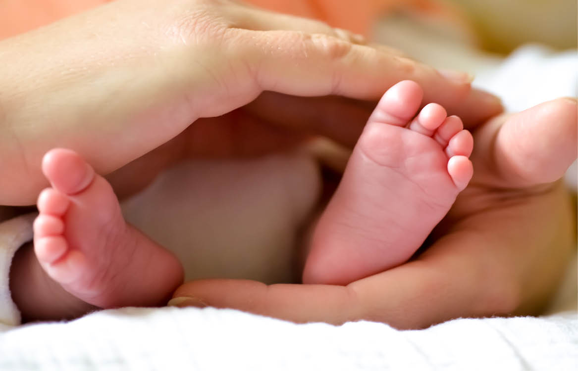 Zwei Hände umfassen liebevoll die Füße eines Babys.